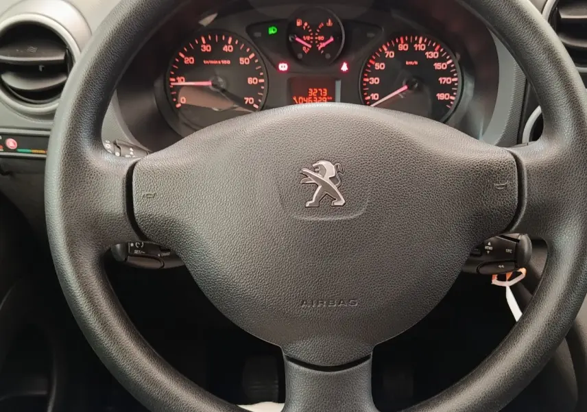 Vue rapprochée du volant noir de Peugeot Partner 1.6 BlueHDi 2018 avec tableau de bord et compteurs rouges en arrière-plan.