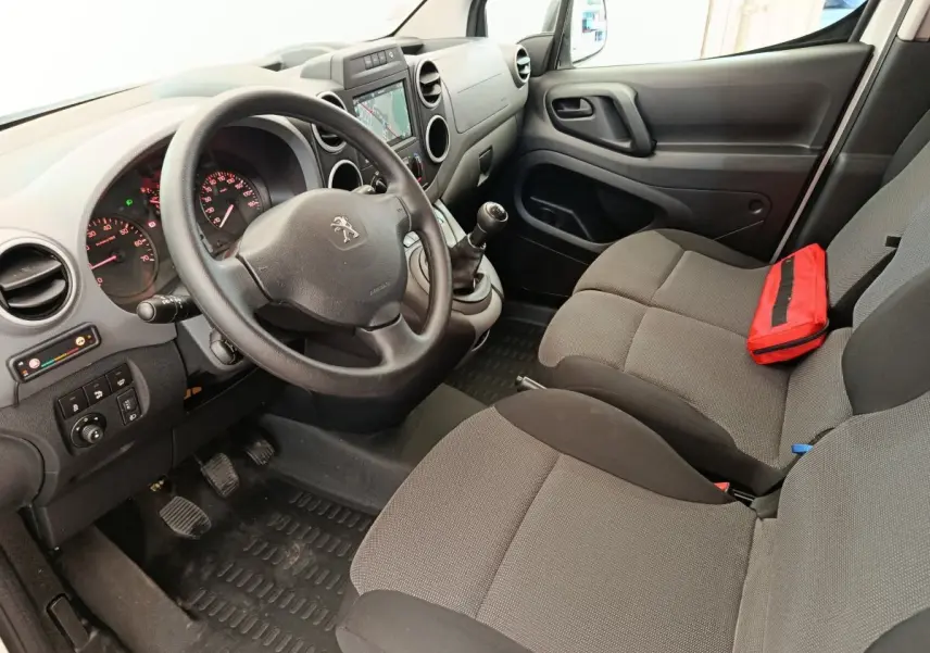 Vue intérieure côté conducteur du Peugeot Partner blanc, montrant le volant, tableau de bord et sièges gris avec trousse rouge.
