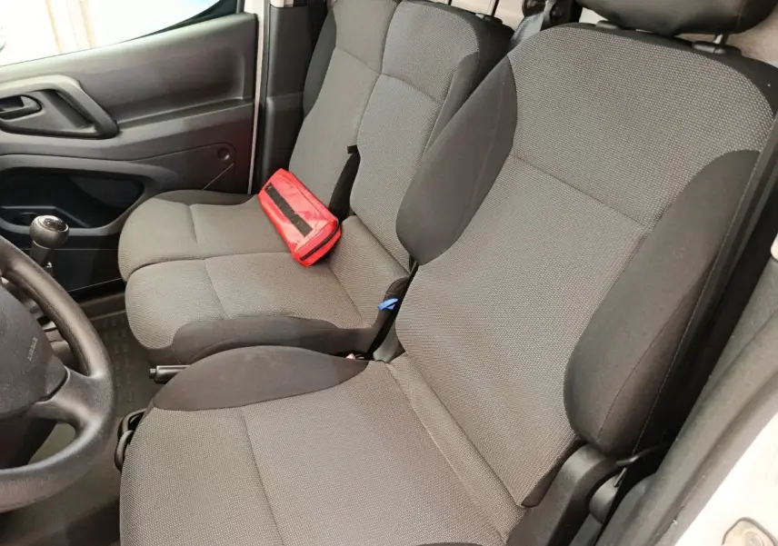 Vue intérieure côté conducteur du Peugeot Partner 1.6 BlueHDi 100, sièges tissu gris avec trousse de secours rouge posée.