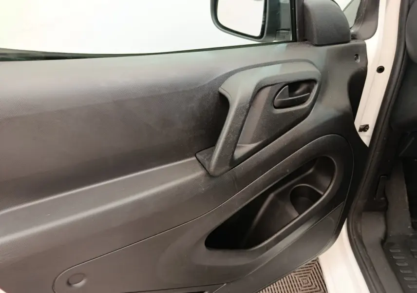 Vue rapprochée de la porte avant gauche noire du Peugeot Partner blanc, avec poignée intégrée et rangement.