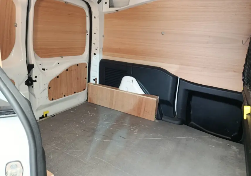 Vue intérieure arrière du Peugeot Partner blanc 2018, montrant l'espace de chargement avec cloison bois et protections latérales.