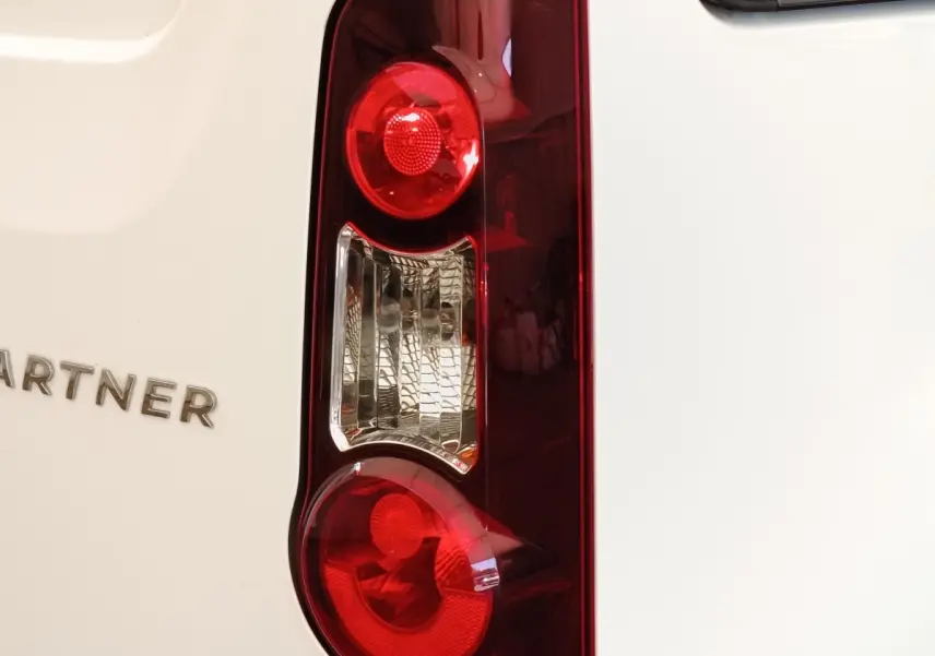 Gros plan sur le feu arrière droit rouge et blanc du Peugeot Partner blanc, avec le logo PARTNER visible sur la carrosserie.
