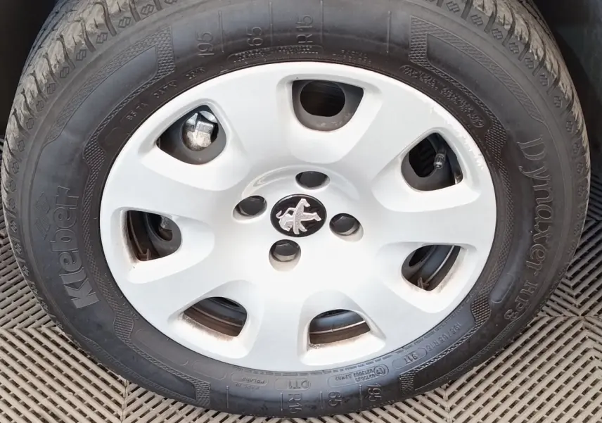 Gros plan sur la roue avant droite avec jante acier blanche et logo Peugeot central visible.