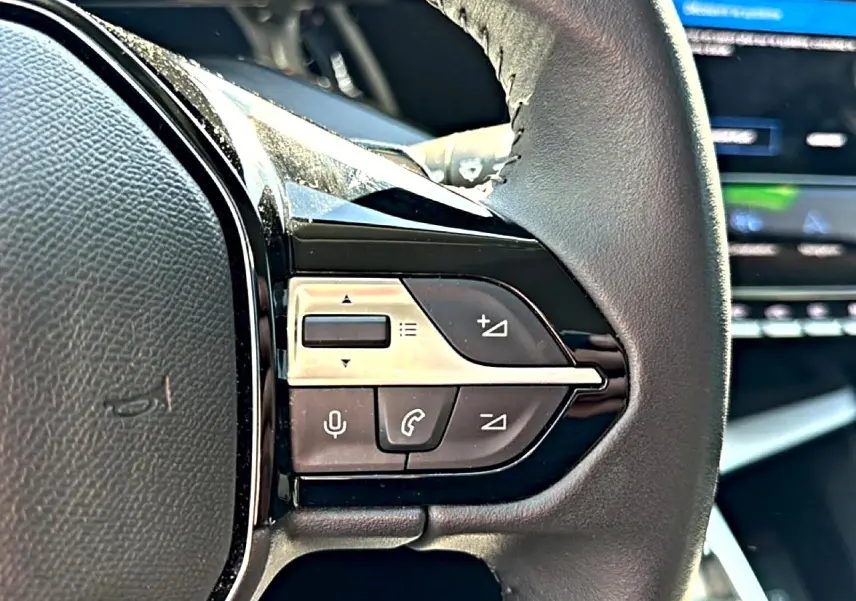 Gros plan sur les commandes du volant cuir noir de la Peugeot 408 Hybrid 145 allure e-dcs6, avec boutons multifonctions.