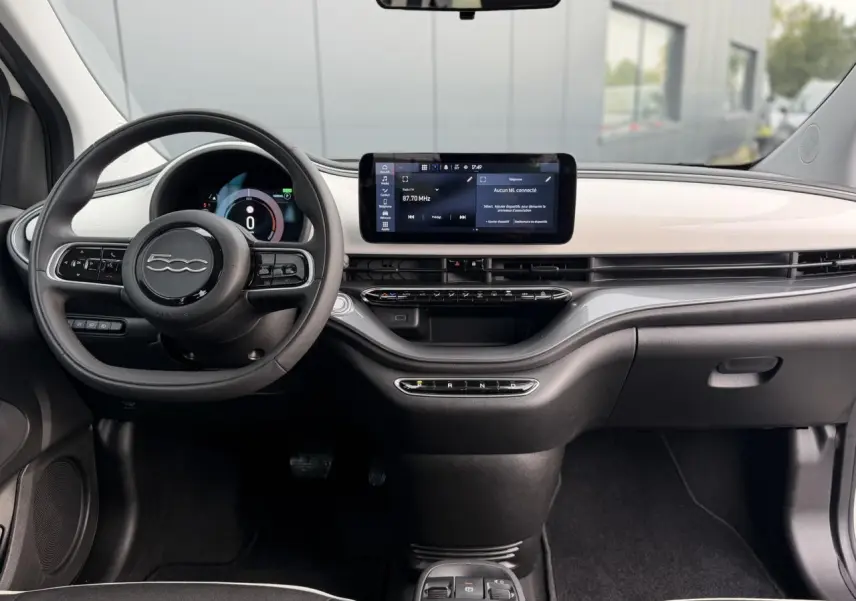 Vue intérieure avant du tableau de bord blanc et noir de la Fiat 500 électrique 2024 avec écran tactile central et volant compact.