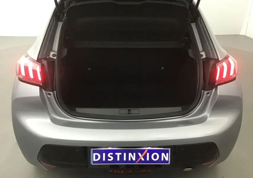 Vue arrière d'une Peugeot 208 1.2 PureTech 100 GT S&S gris Artense avec coffre ouvert et feux arrière allumés.