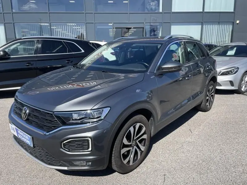 Volkswagen T-Roc gris foncé métal vu de 3/4 avant droit, avec jantes alliage et calandre noire distinctive.