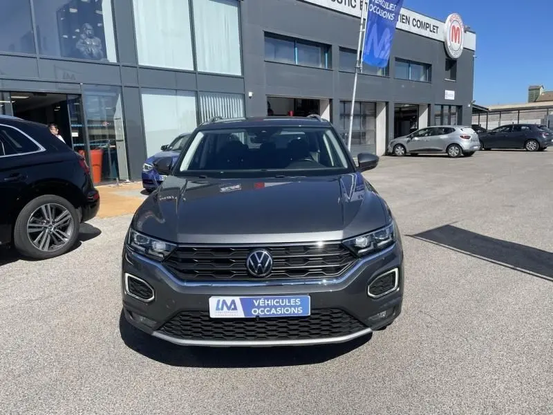 Volkswagen T-Roc gris foncé métal vu de face, avec calandre noire et plaque "Véhicules Occasions" visible.