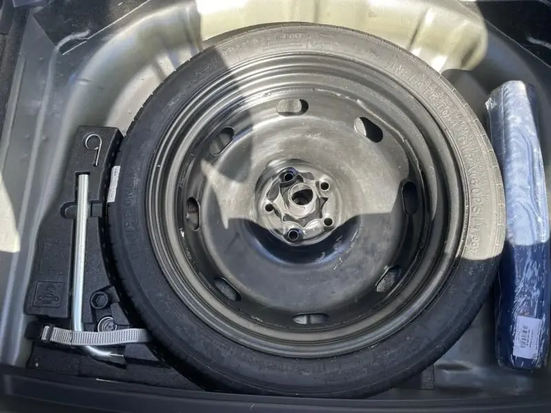 Roue de secours en acier noir avec cric et outils dans le coffre d'un Volkswagen T-Roc gris foncé 2021.