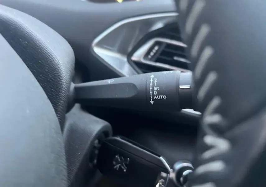 Gros plan sur la manette d’essuie-glace et la clé de contact du tableau de bord intérieur d’une Peugeot 308 blanche.