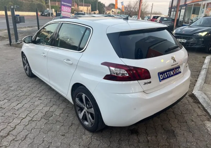 Peugeot 308 blanche vue 3/4 arrière côté gauche, avec toit panoramique et jantes alliage distinctives.
