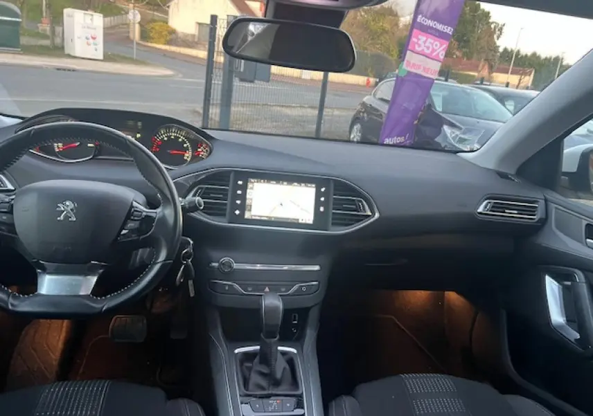 Intérieur de Peugeot 308 blanc 2017 vu de face, tableau de bord avec écran tactile de navigation allumé.