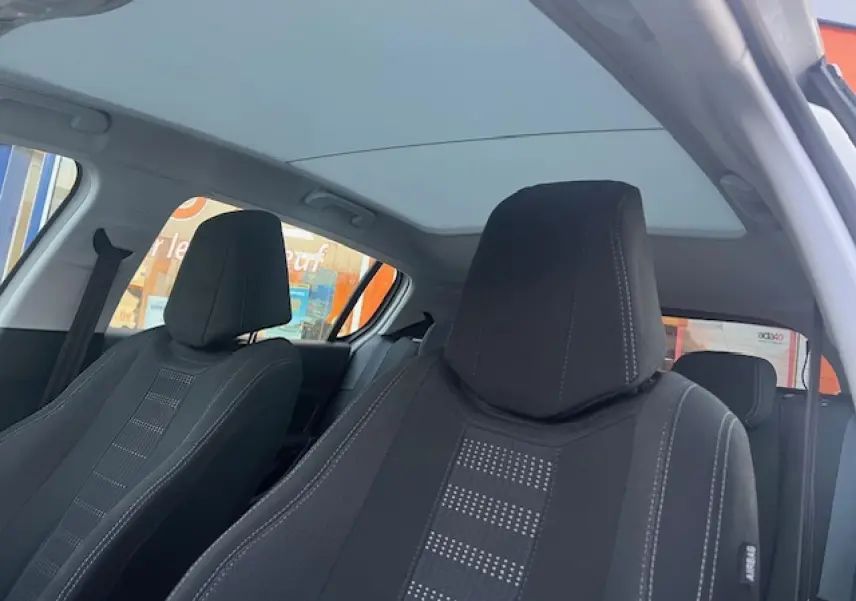 Vue intérieure des sièges avant noirs et du toit panoramique fermé d'une Peugeot 308 blanche.