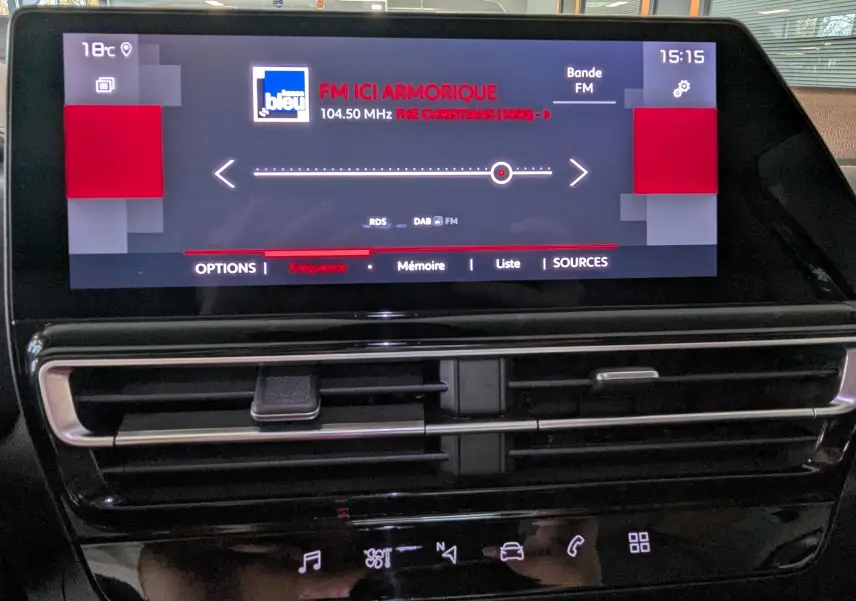 Écran tactile central du tableau de bord du Citroën C5 Aircross hybride 2024 affichant la radio FM et commandes climatisation.