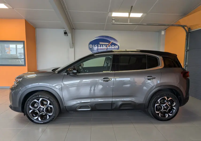Profil côté gauche du Citroën C5 Aircross hybride gris platinium avec jantes alliage 18 pouces en intérieur showroom.
