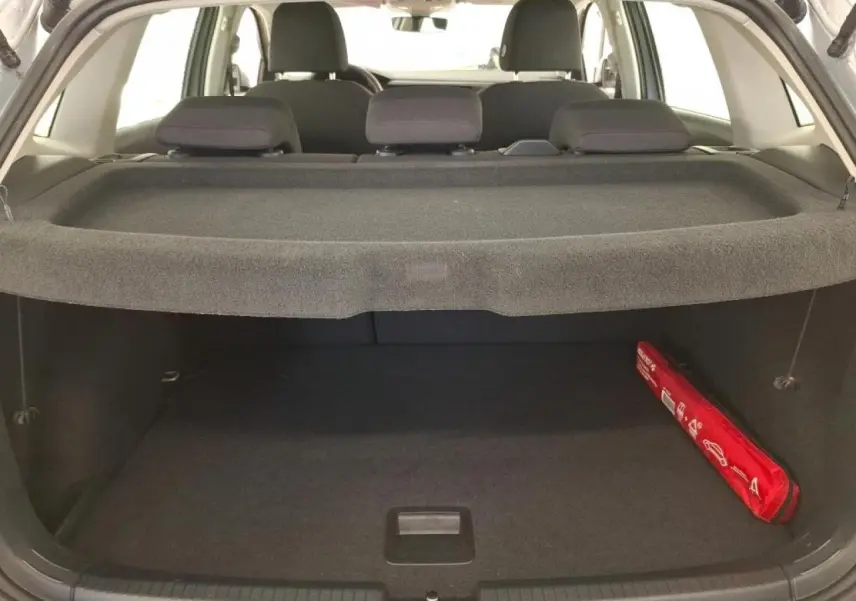 Vue arrière du coffre ouvert d'une Volkswagen Polo gris clair, avec cache-bagages et trousse de sécurité rouge sur le côté droit.
