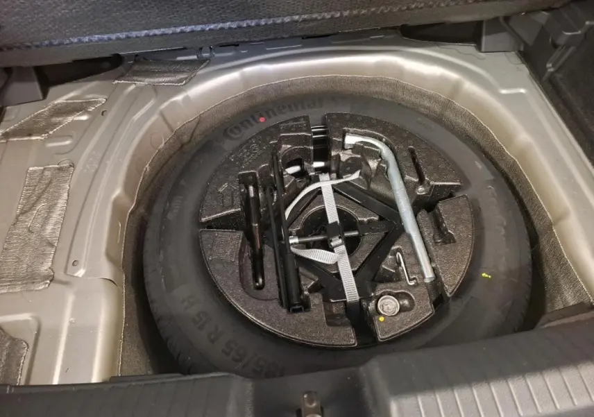 Vue rapprochée de la roue de secours acier 15 pouces et outillage de bord dans le coffre d'une Volkswagen Polo gris clair.