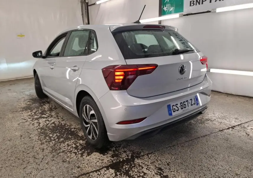 Volkswagen Polo gris clair vue 3/4 arrière droit avec feux arrière allumés en intérieur.