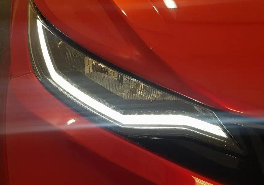 Gros plan sur le phare avant gauche allumé de l'AIXAM Ambition 0.5 City Pack rouge 2026, avec carrosserie brillante.