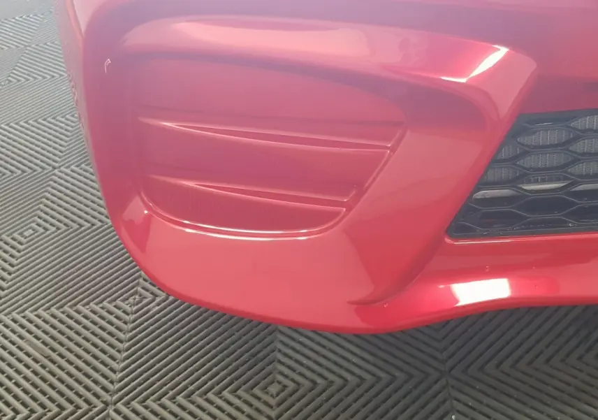 Gros plan sur le pare-chocs avant rouge de l'AIXAM AMBITION 0.5 CITY PACK avec grille noire visible à droite.