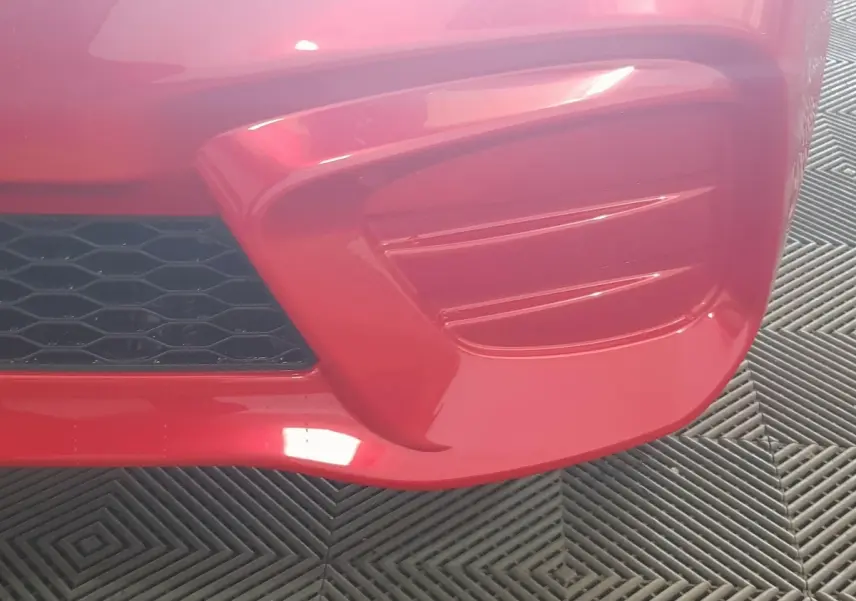 Gros plan sur le pare-chocs avant rouge de l'AIXAM AMBITION 0.5 CITY PACK avec grille noire et détails profilés.