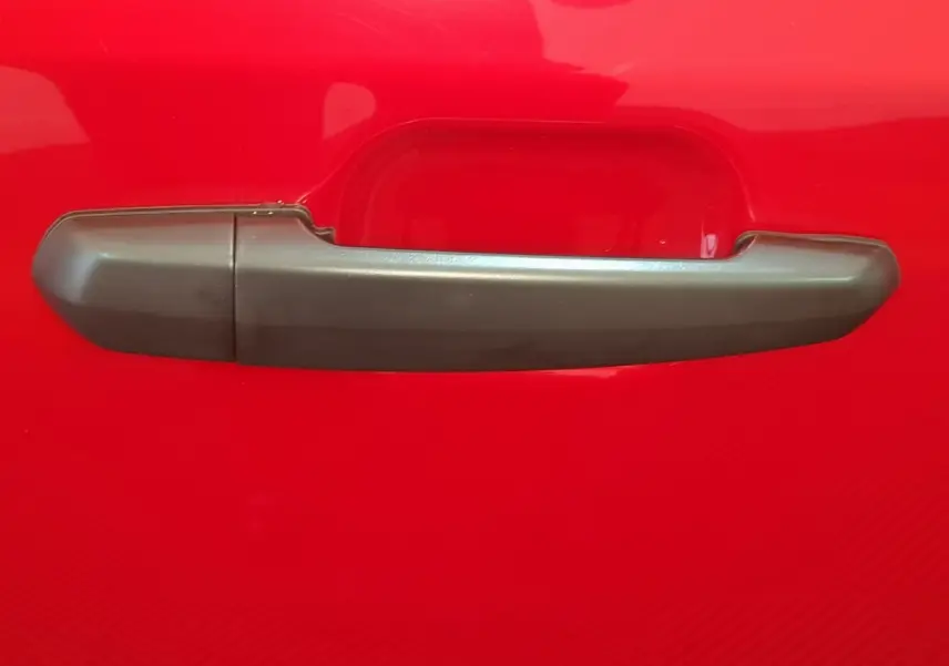 Poignée de porte grise sur la portière rouge d'une Aixam Ambition 0.5 City Pack 2026, vue en gros plan.