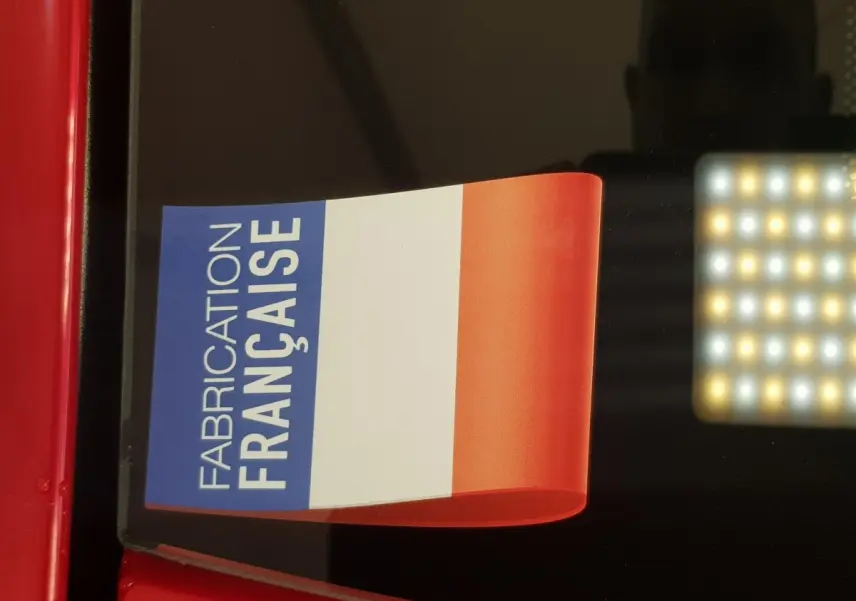 Gros plan sur l'autocollant tricolore "Fabrication Française" sur la carrosserie rouge d'une Aixam Ambition 0.5 City Pack.