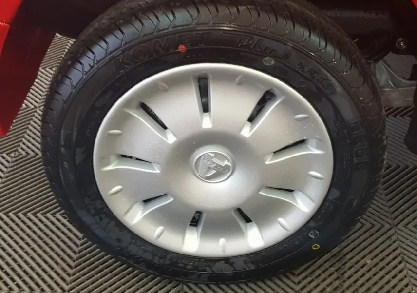 Gros plan sur la roue avant droite d’une Aixam Ambition 0.5 City Pack rouge, avec enjoliveur argenté et logo central.