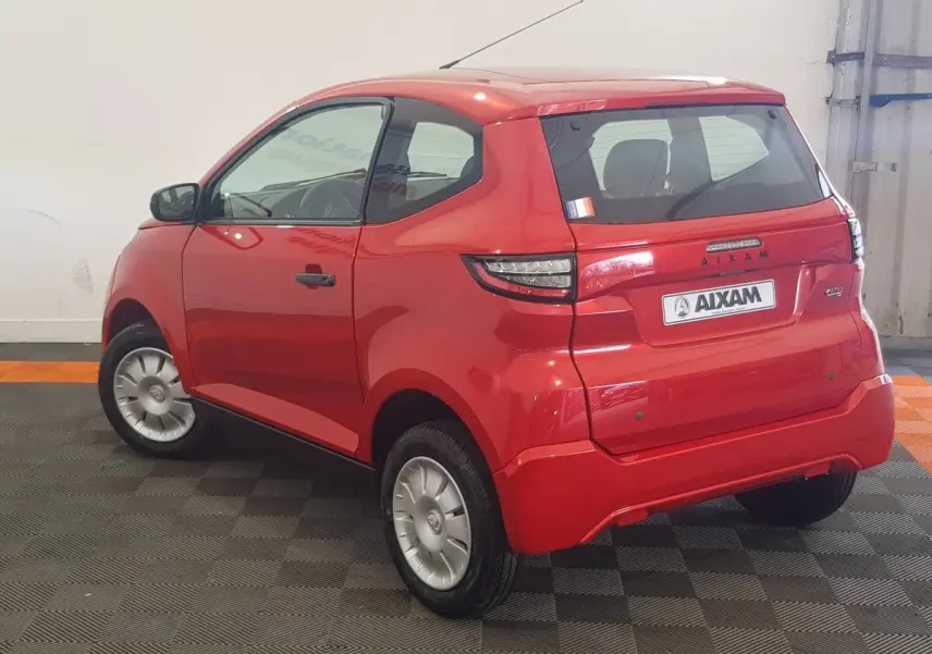 Vue 3/4 arrière droite d'une Aixam Ambition 0.5 City Pack rouge 2026 avec caméra sur rétroviseur côté gauche.