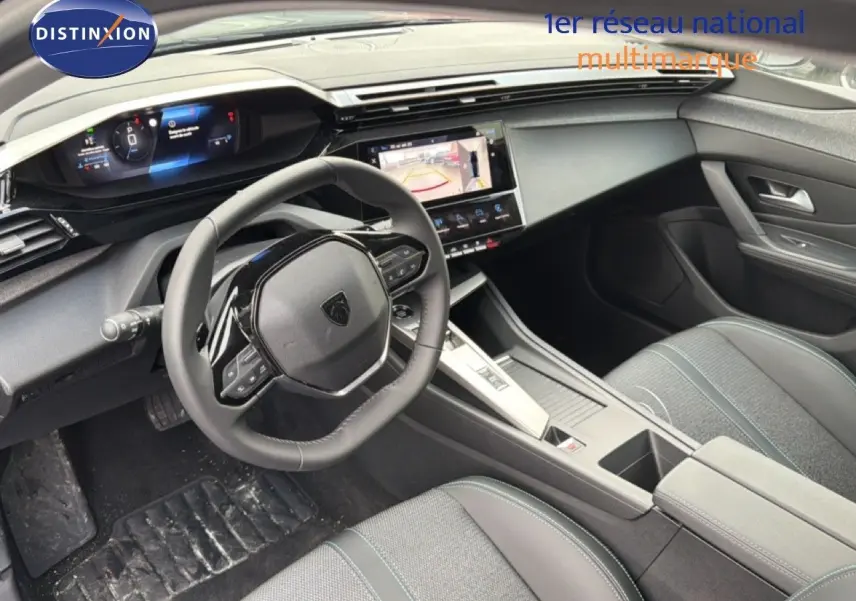 Vue intérieure côté conducteur de la Peugeot 308 hybride 2025 avec tableau de bord numérique et sellerie noire tissu et cuir.