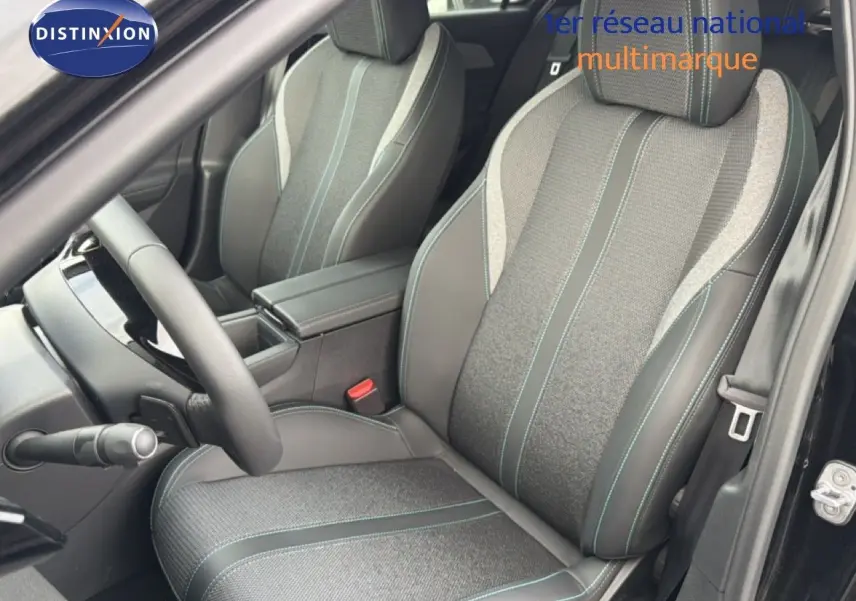 Vue intérieure côté conducteur de la Peugeot 308 1.2 Hybrid 2025, sièges tissu et cuir noir avec surpiqûres bleues.