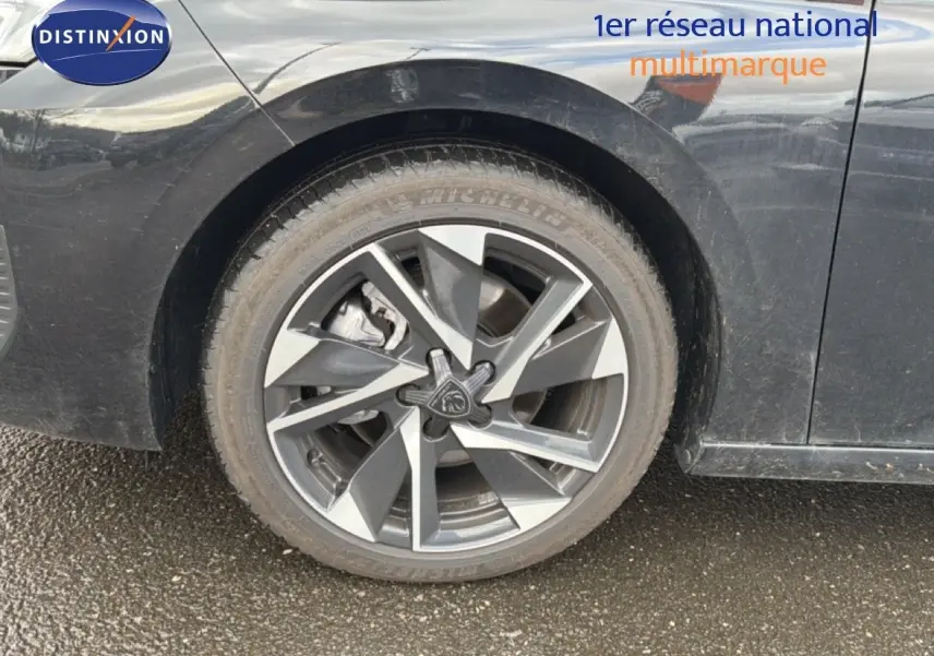 Gros plan sur la roue avant gauche d'une Peugeot 308 noire métal, mettant en valeur la jante alliage au design moderne.