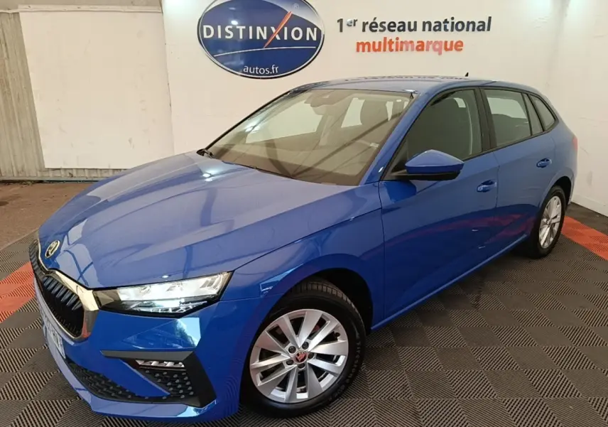 SKODA SCALA 1.5 TSI bleu vue 3/4 avant droit, jantes alliage et calandre chromée visible en intérieur showroom.