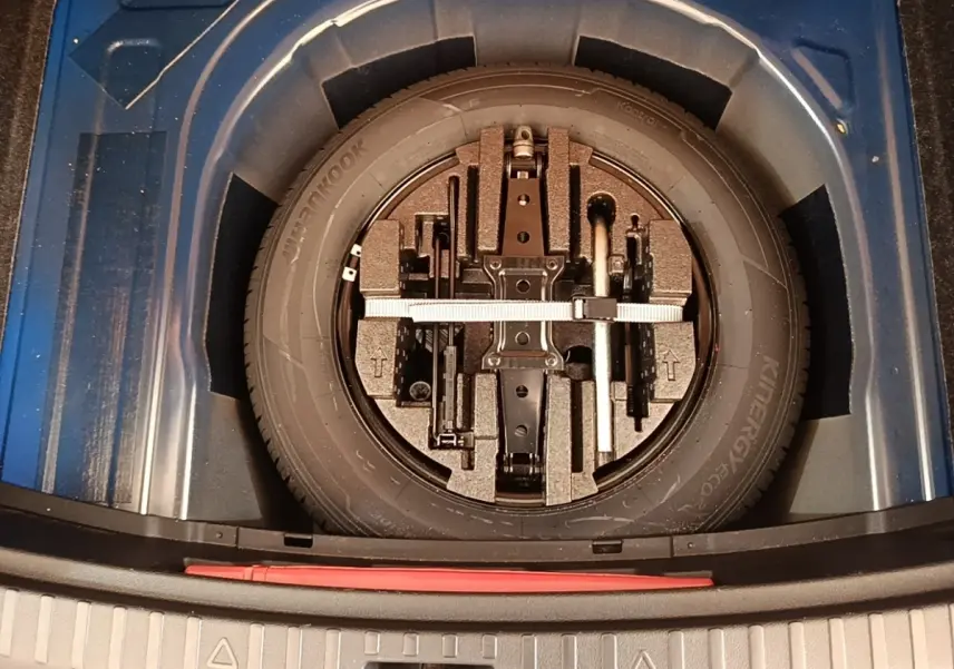 Vue plongeante sur la roue de secours galette et outils dans le coffre d'une Skoda Scala bleu 2024.