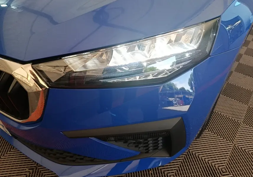 Gros plan sur l'avant droit bleu d'une Skoda Scala 2024, mettant en valeur le phare LED et la calandre chromée.