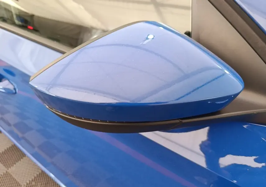 Rétroviseur côté gauche bleu métallisé de la SKODA SCALA 1.5 TSI 2024, avec carrosserie et poignée assorties visibles.