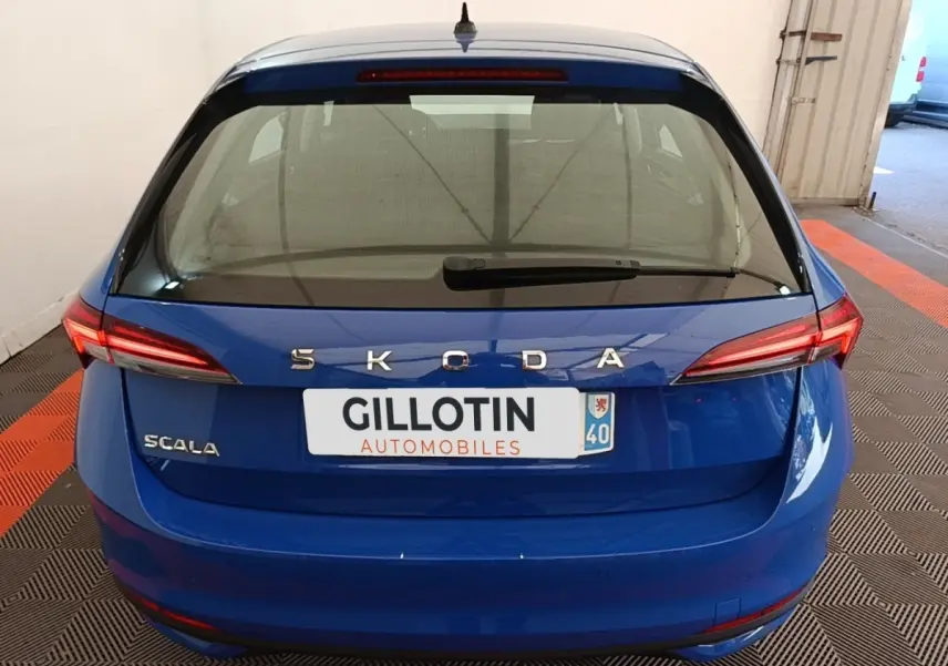 Vue arrière d'une Skoda Scala bleue 2024 avec feux LED et logo SKODA bien visibles sur un sol à damier noir et orange.