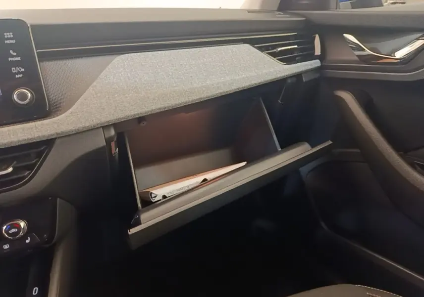 Intérieur de la Skoda Scala 2024, vue côté passager sur la boîte à gants ouverte avec tableau de bord gris et noir.