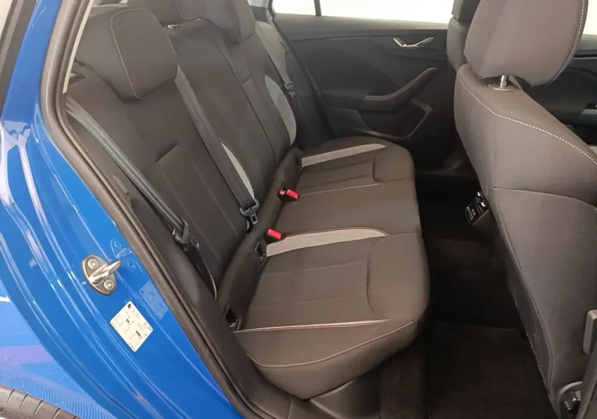 Vue intérieure côté gauche sur la banquette arrière noire avec surpiqûres et portière bleu vif ouverte d’une Skoda Scala 2024.