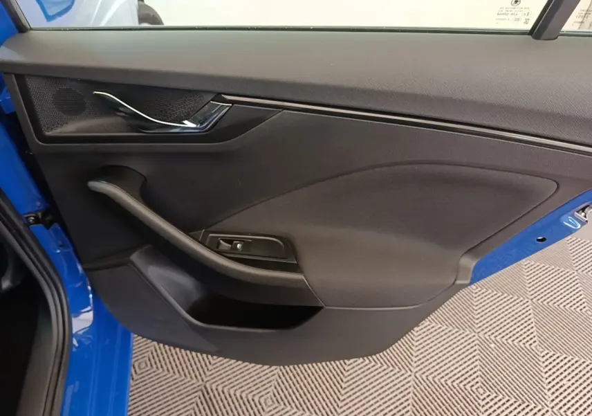 Vue intérieure côté gauche de la porte avant d'une Skoda Scala 2024 bleue avec poignée chromée et bouton de lève-vitre.