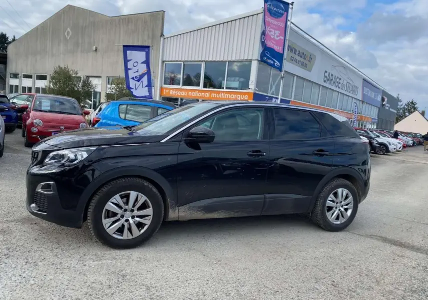 Peugeot 3008 noir vue de profil côté gauche, avec des traces de boue sur les bas de caisse, stationné devant un garage.