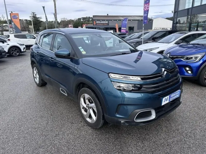 Vue 3/4 avant d'un Citroën C5 Aircross bleu Tijuca 2021 avec détails de calandre et jantes visibles sur parking.