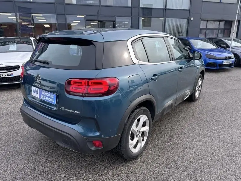 Vue 3/4 arrière droite d'un Citroën C5 Aircross bleu Tijuca avec toit noir et feux arrière distinctifs, stationné en extérieur.
