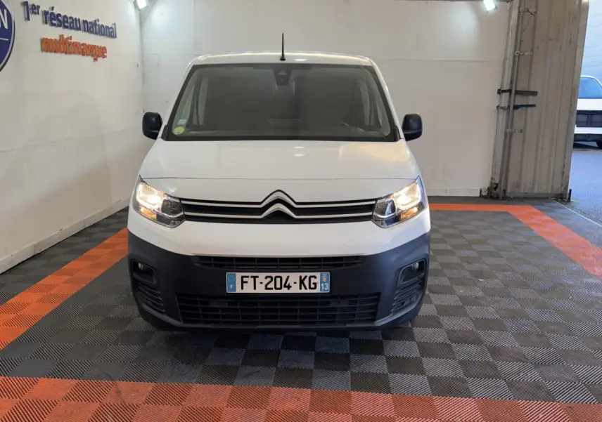 Vue avant d'un Citroën Berlingo blanc 2020 avec calandre noire et phares allumés dans un garage.
