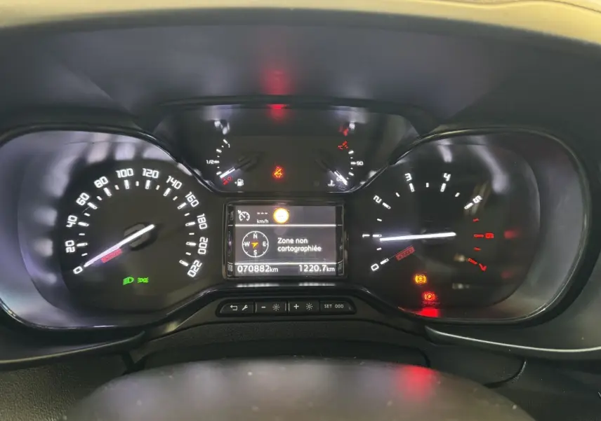 Vue rapprochée du tableau de bord digital du Citroën Berlingo blanc, affichant la navigation et compteurs allumés.