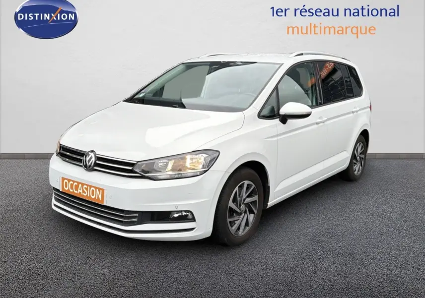 Volkswagen Touran blanc en 3/4 avant droit avec jantes alliage et feux allumés sur fond neutre.