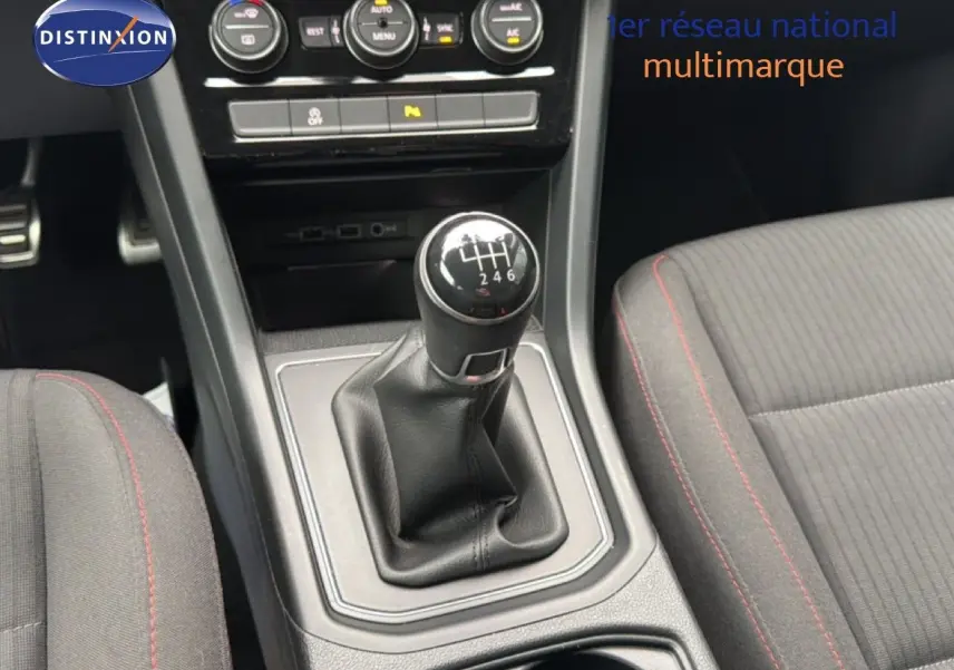 Gros plan sur le levier de vitesses manuel noir et la console centrale du Volkswagen Touran 2018, avec sièges tissu gris à surpiqûres rouges.