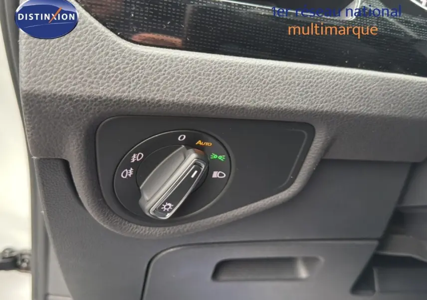 Détail du bouton de commande des phares sur le tableau de bord du Volkswagen Touran blanc, vue intérieure côté conducteur.