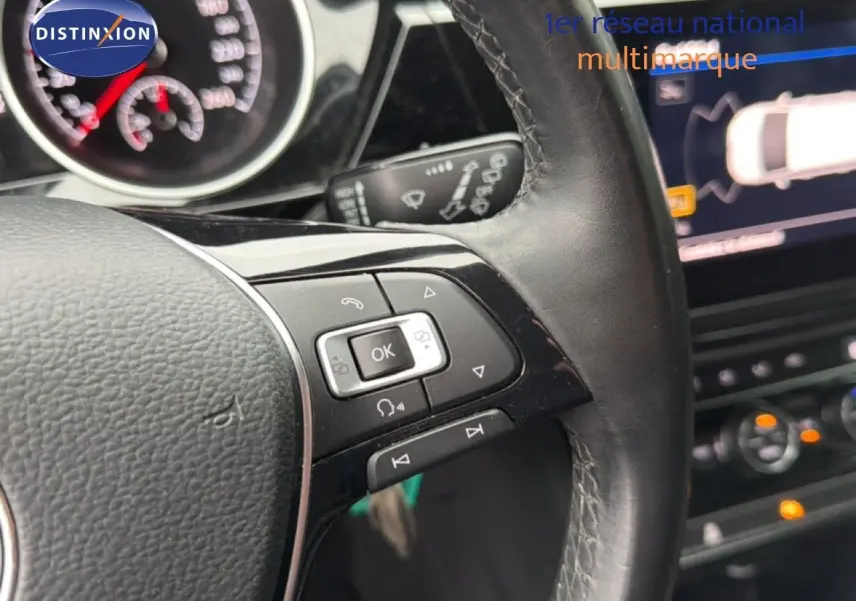 Gros plan sur le volant en cuir noir du Volkswagen Touran 2018 avec commandes intégrées et tableau de bord numérique en arrière-plan.