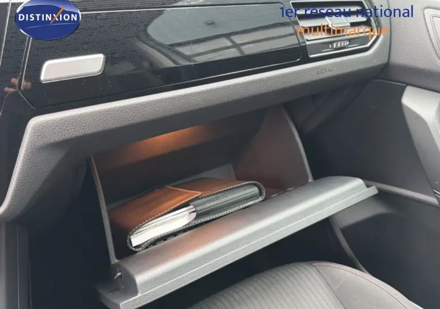 Vue intérieure du coffre à gants ouvert côté passager du Volkswagen Touran blanc, avec un carnet à l'intérieur.